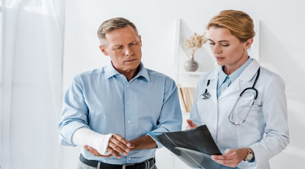 attractive doctor gesturing near man with broken arm and looking at x ray